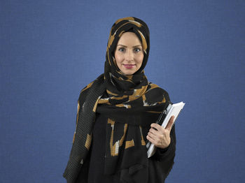 Portrait of young woman standing against blue background