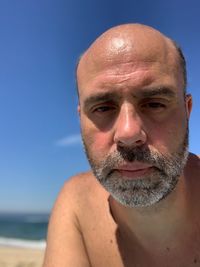 Close-up portrait of shirtless man against clear blue sky at beach