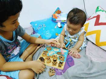High angle view of siblings playing with toys on bed at home