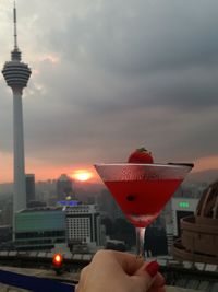 Close-up of hand holding red wine and tower against sky in city