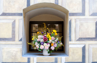 Bouquet of wild flowers and annual summer flowers in vase at window sill of historic building