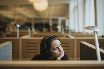 Contemplative young female student with hand on chin sitting in library at university