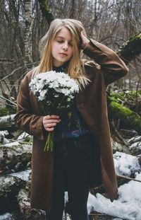 Young woman holding bouquet against tree trunks