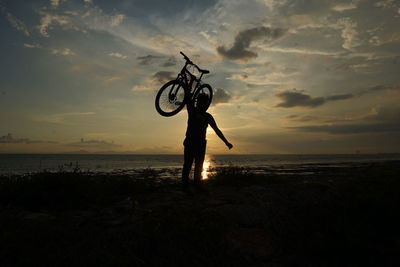 Silhouette man with bicycle on beach against sky during sunset