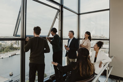 Cheerful male and female colleagues looking through window while celebrating at office party