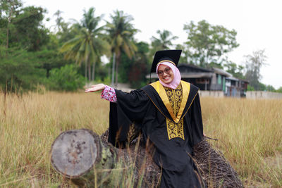 Woman in graduation gown sitting on log