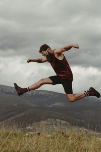 Woman jumping on field against sky