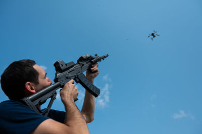 Low angle view of man holding drone against clear sky