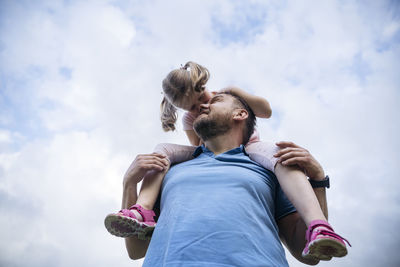 Father carrying daughter on shoulders under sky