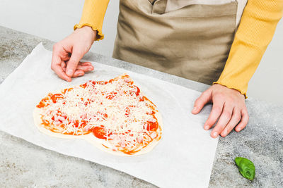 Hand of caucasian teenage girl pouring grated cheese on pizza hearts for valentine's day.