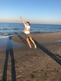 Full length of girl jumping at beach against sky
