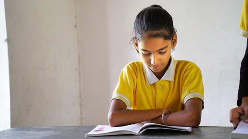 Portrait of happy indian school child sitting at desk in classroom, school kids with pens 