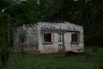 Old abandoned house on field against trees