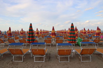 Empty chairs on beach against sky