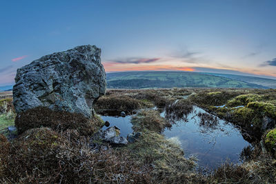 Rock formation by lake against sky during sunset