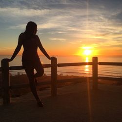 Woman standing at beach against sky during sunset