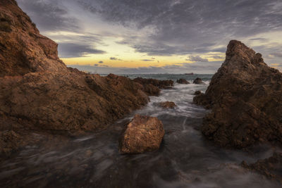 Rocks in sea against sky during sunset