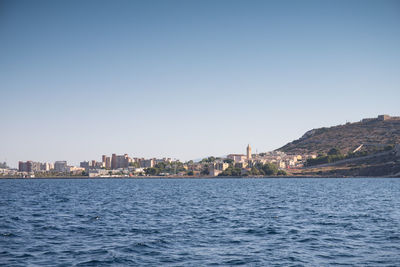 Sea by buildings against clear blue sky