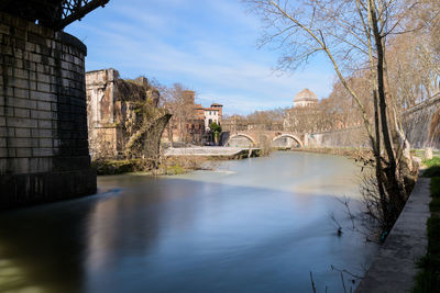 Arch bridge over river amidst buildings against sky