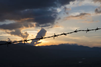 Barbed wire fence against sky during sunset