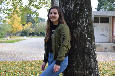 Portrait of smiling young woman standing on tree trunk