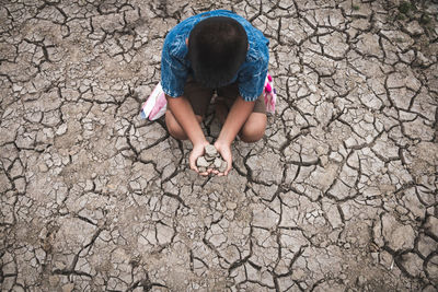 High angle view of boy sitting on drought land