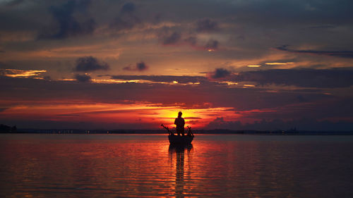 Silhouette man in sea against sky during sunset