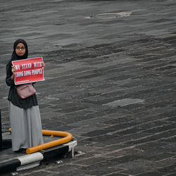 Woman holding paper with text while standing on footpath