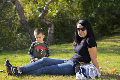 Smiling mother and son sitting on grass against trees