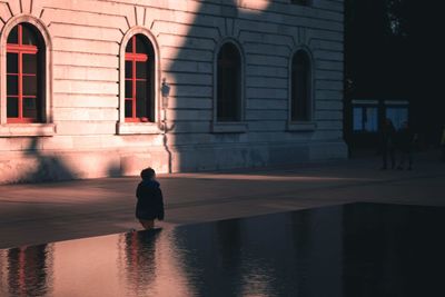 Rear view of silhouette man walking on street against building