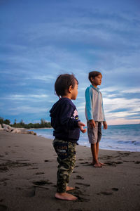 Boy standing on beach against sky