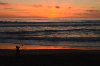 Silhouette man standing on beach against orange sky