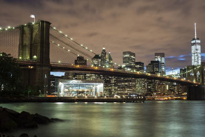 Illuminated bridge over river with city in background