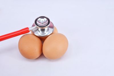 Close-up of eggs and stethoscope on white background