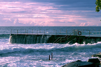 Scenic view of sea waves against cloudy sky during sunset