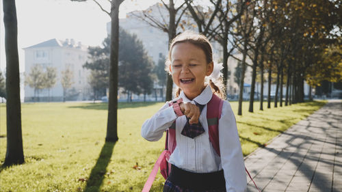 Cheerful schoolgirl walking on footpath amidst trees in park