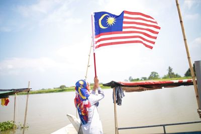 Flags on boat in river against sky