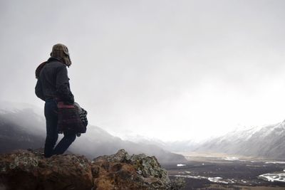 Rear view of man standing on rock against sky