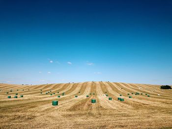 Hay bales on field against blue sky