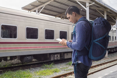 Side view of tourist using digital tablet while standing at railroad station platform