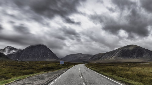 Empty road in glencoe leading towards mountains against sky