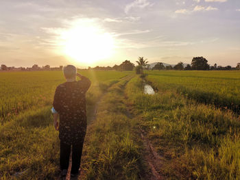 Rear view of woman walking on field against sky during sunset