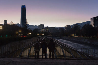 Rear view of people on illuminated buildings against sky at dusk