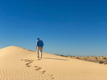 Rear view of man walking on sand in desert against sky