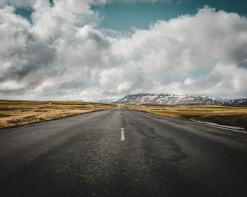 Road amidst field against cloudy sky