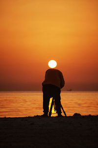 Rear view of man with tripod at beach during sunset