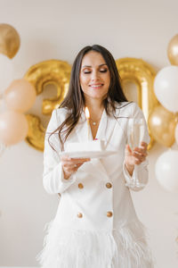 Young caucasian woman holding a cake with a candle and a glass of champagne in honor of the birthday
