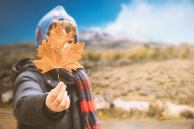 Cute boy holding maple leaf while standing on field during autumn