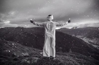 Rear view of man with arms outstretched standing on mountain against sky