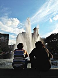 Rear view of men sitting against fountain at washington square park